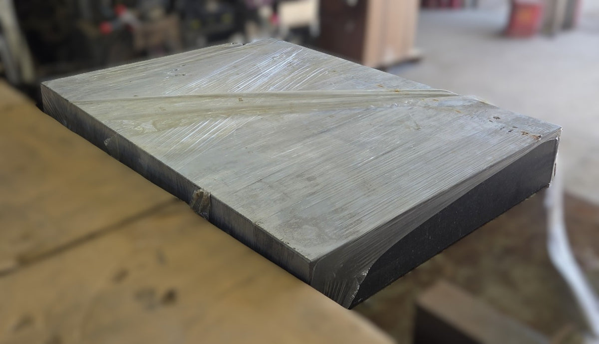 Elevated corner view of the plastic-wrapped metrology surface plate highlighting the straight machined edges and overall massive footprint.
