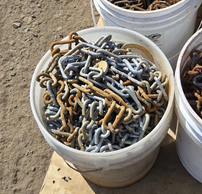 Close-up of a white plastic bucket containing a mix of heavily rusted chain and dull grey galvanized steel chain.