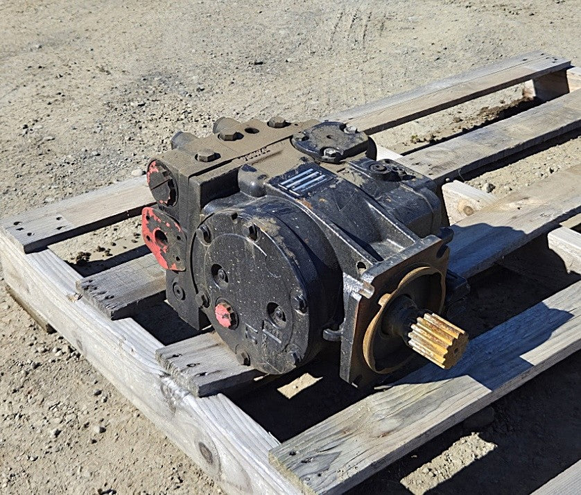  Remanufactured Sauer-Danfoss 90R100 hydraulic pump resting on a wooden pallet showing black casing, 14-tooth splined shaft, and red port plugs.