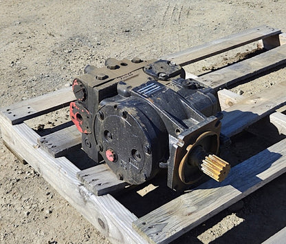  Remanufactured Sauer-Danfoss 90R100 hydraulic pump resting on a wooden pallet showing black casing, 14-tooth splined shaft, and red port plugs.