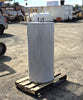 Tall grey Bradford White cylindrical electric water heater resting on a wooden pallet in a dirt equipment yard