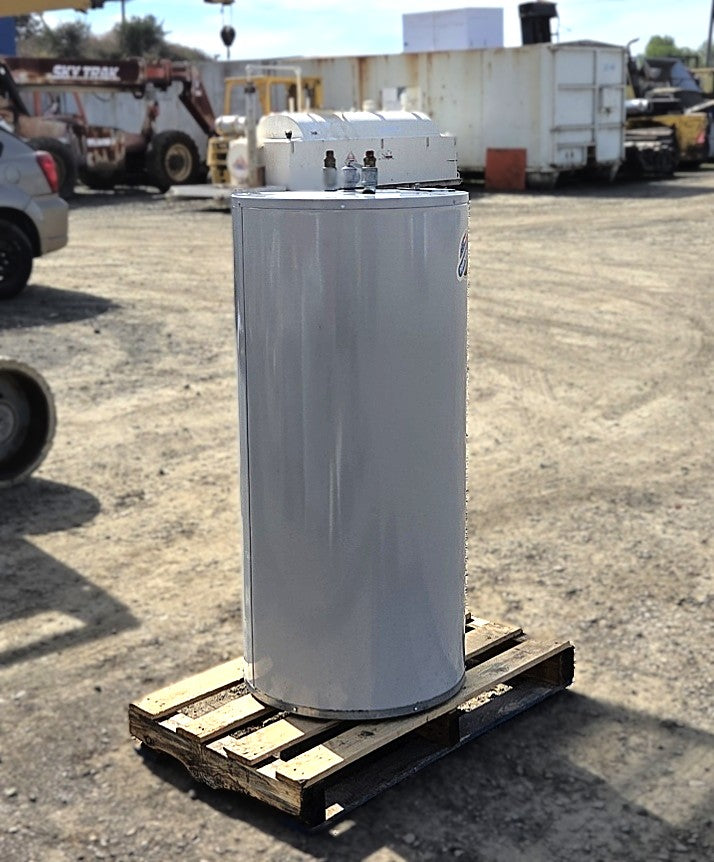 Tall grey Bradford White cylindrical electric water heater resting on a wooden pallet in a dirt equipment yard