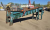 Front angle view of the green West Coast Industrial Systems incline conveyor showing the wide rubber belt, orange drum pulley, and manual take-up bearing.