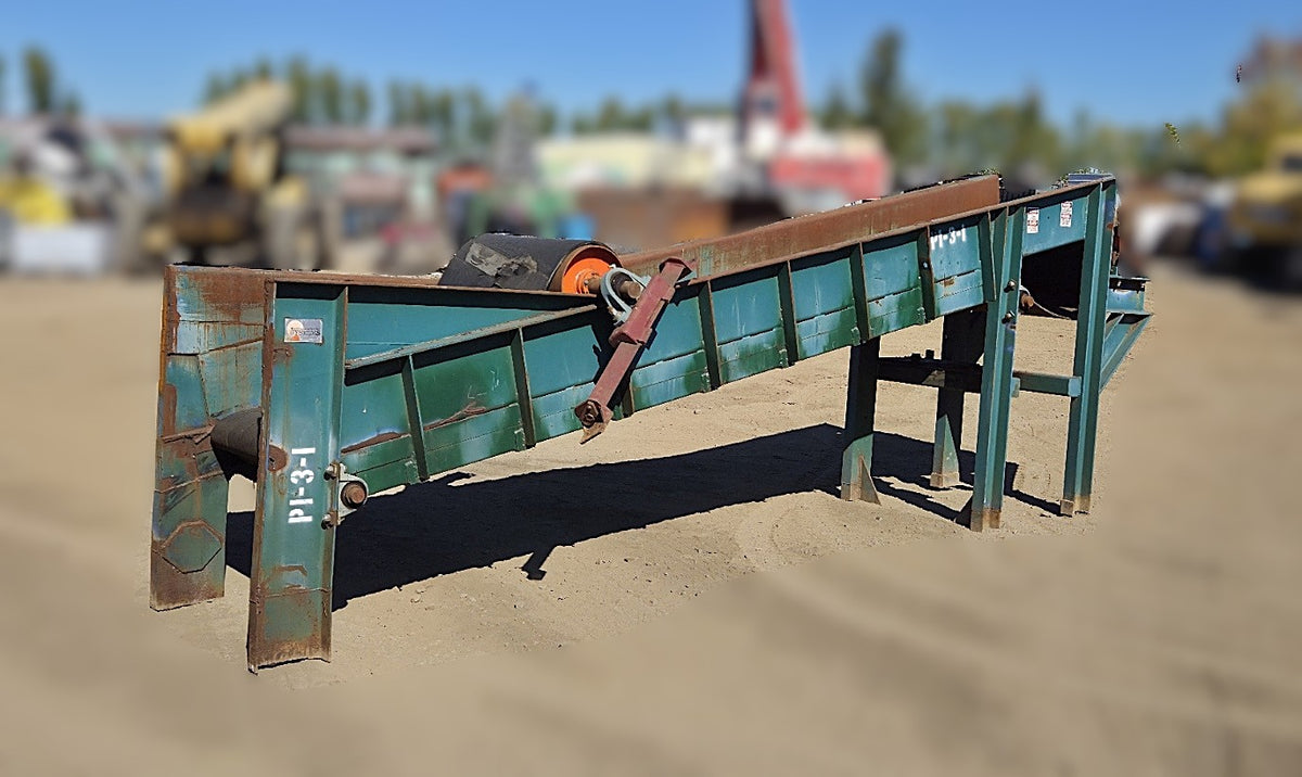 Front angle view of the green West Coast Industrial Systems incline conveyor showing the wide rubber belt, orange drum pulley, and manual take-up bearing.