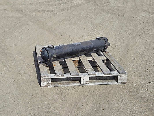 Sullair shell and tube heat exchanger resting on a wooden pallet showing the long black cylindrical steel shell and mounting saddles.