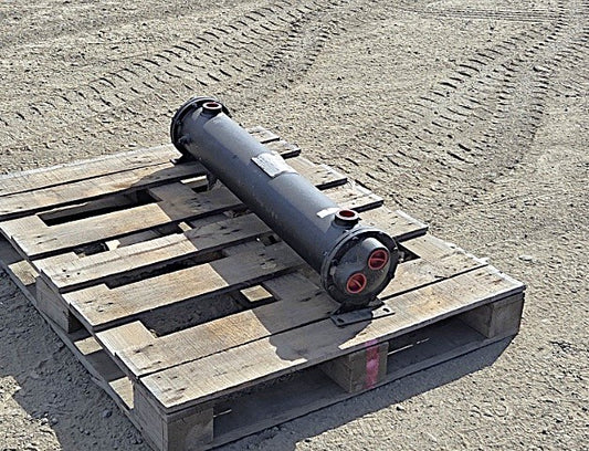 Sullair 02250120-863 shell and tube heat exchanger resting on a wooden pallet showing the long black cylindrical steel shell and mounting saddles. 