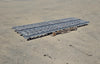 Wide side-angle view of two 10-foot galvanized steel gravity skatewheel conveyor sections resting flat on a wooden pallet in an outdoor yard.
