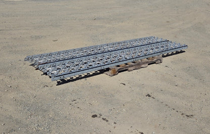 Wide side-angle view of two 10-foot galvanized steel gravity skatewheel conveyor sections resting flat on a wooden pallet in an outdoor yard.
