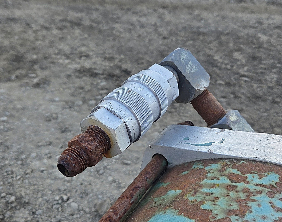 Close-up of a silver FLO-SET quick-disconnect fitting and threaded port on the green pneumatic cylinder showing surface rust.
