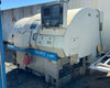 An industrial CNC lathe machine by Okuma, model Crown L1060, with a large white metal body, blue brand name panels, and a dark gray control console mounted on top, photographed outdoors against a concrete wall.